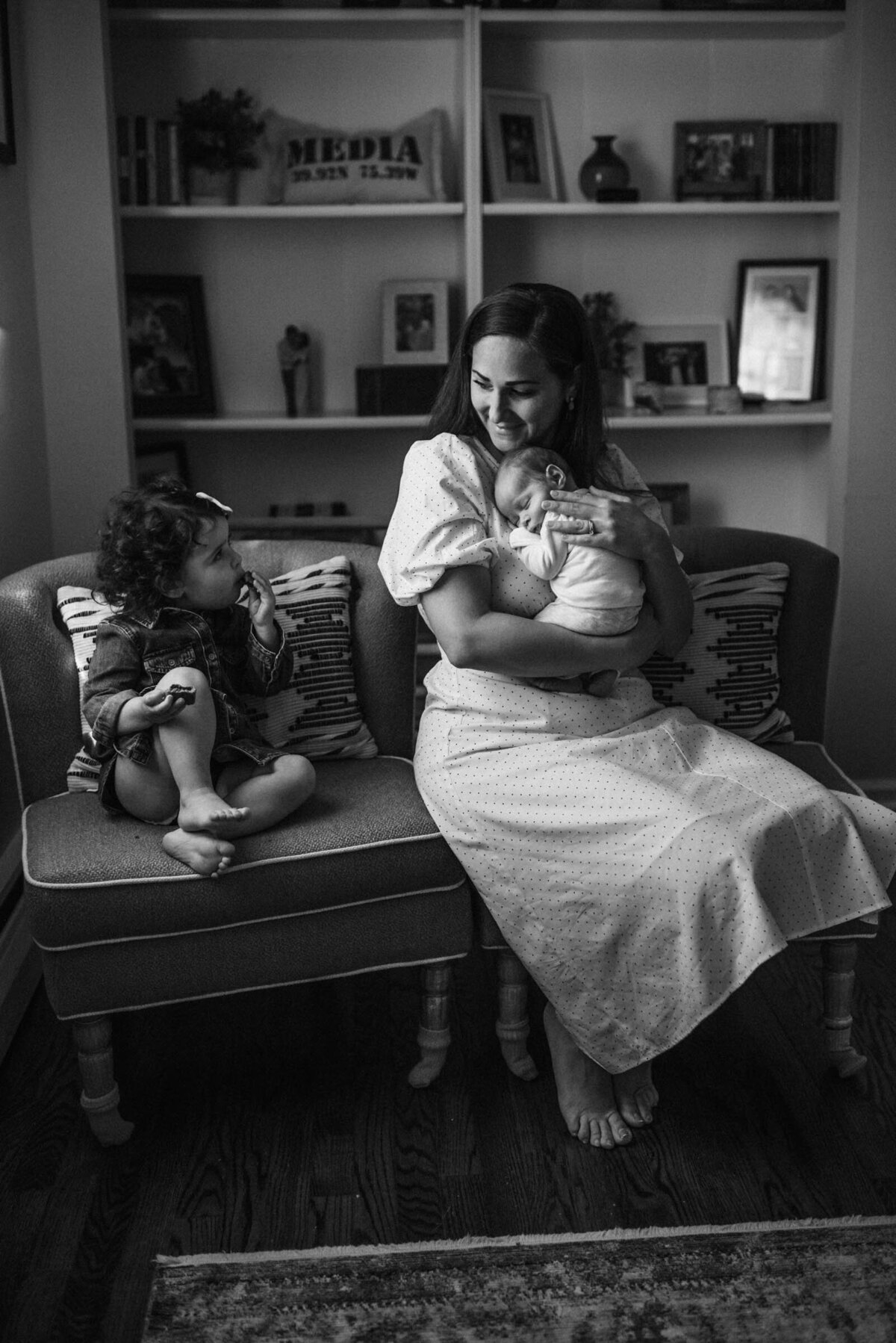 Child takes a snack break during newborn inhome session while mother waits holding baby Newborn Portrait Photography