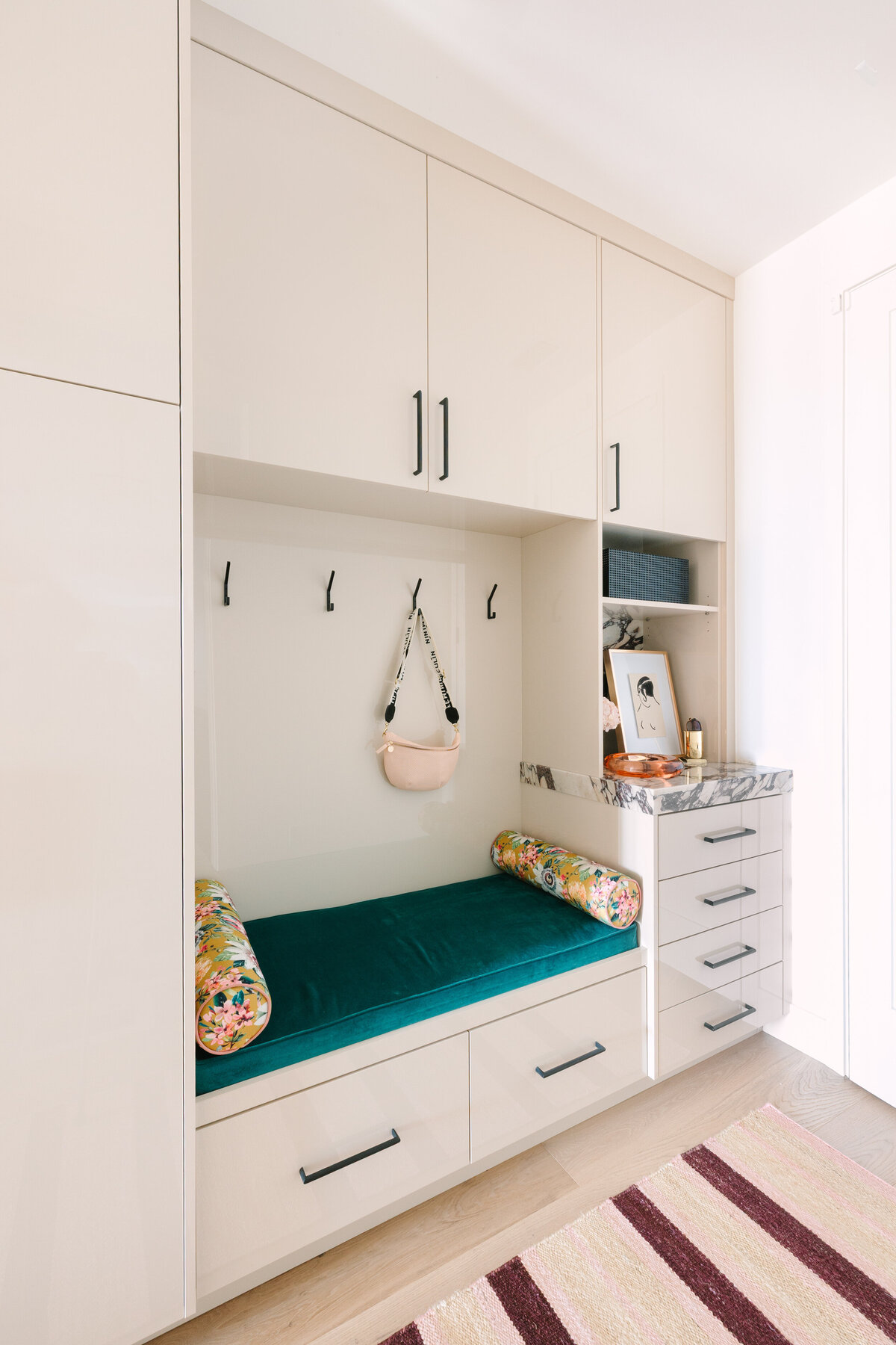 Modern mudroom with beige high gloss cabinets, Calcatta Viola marble counters, and floral cushions.