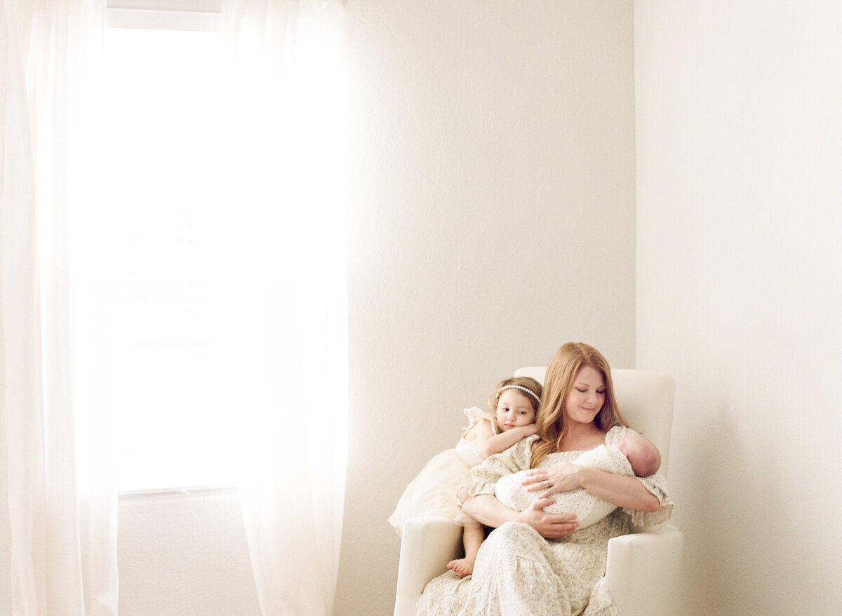 New mom sits in a rocker with her toddler and newborn. Image by Raleigh newborn photographer A.J. Dunlap Photography.