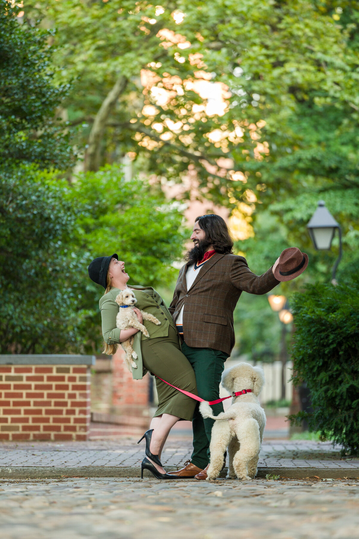 Playful engagement photo of a couple dressed casually, recreating the iconic 101 Dalmatians pose with their two dogs in Old City Philadelphia, showcasing creativity and their love for pets amidst beautiful cobblestone streets.