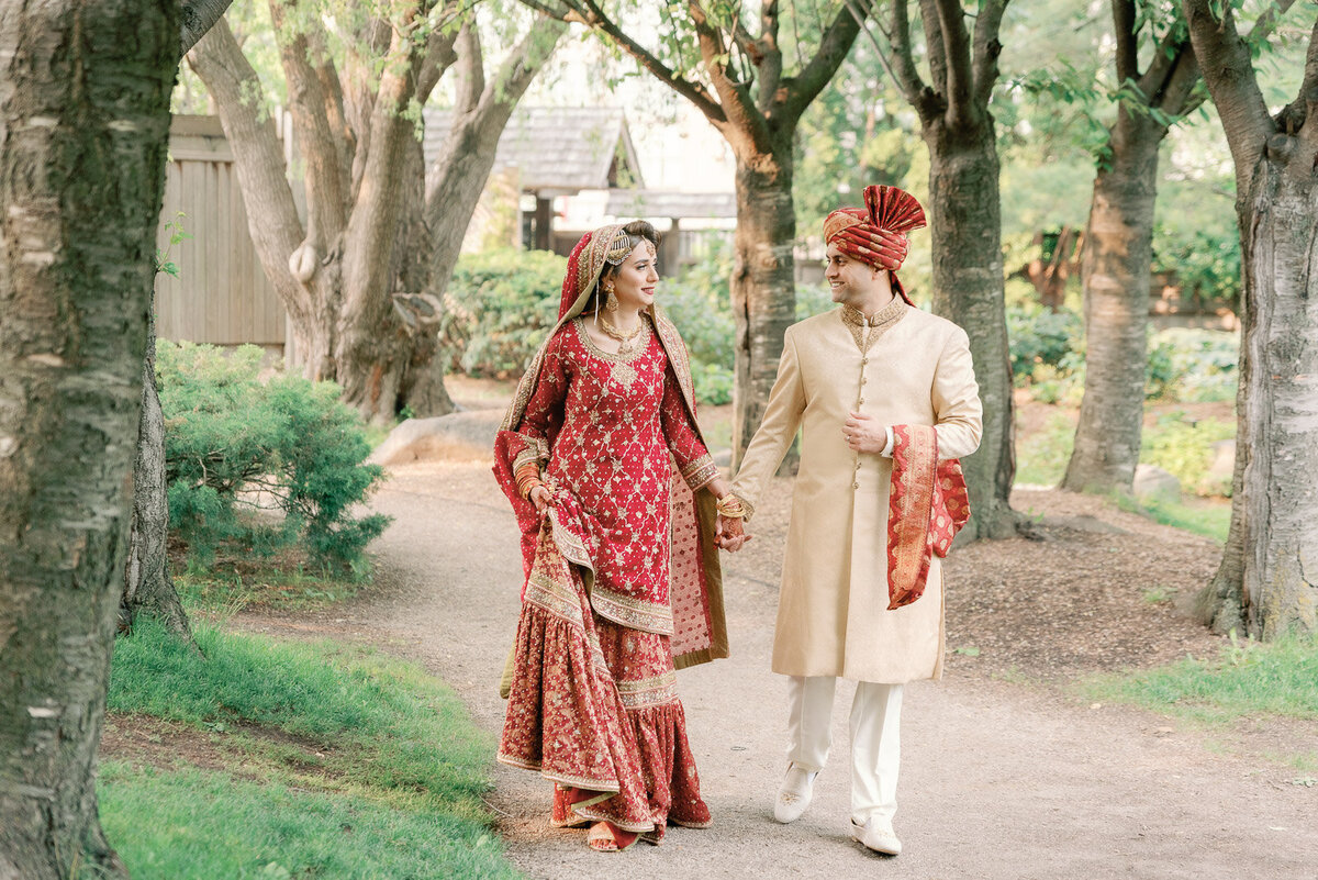 bride and groom holding hands as they walk down a path surrounded by trees and greenery
