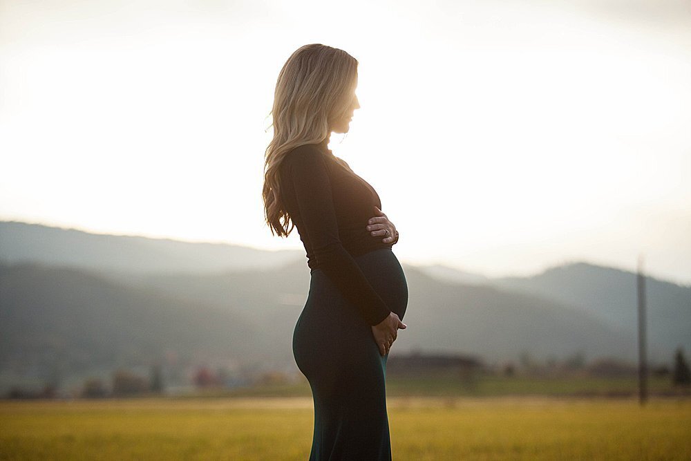pregnant woman holding her tummy in sunset light