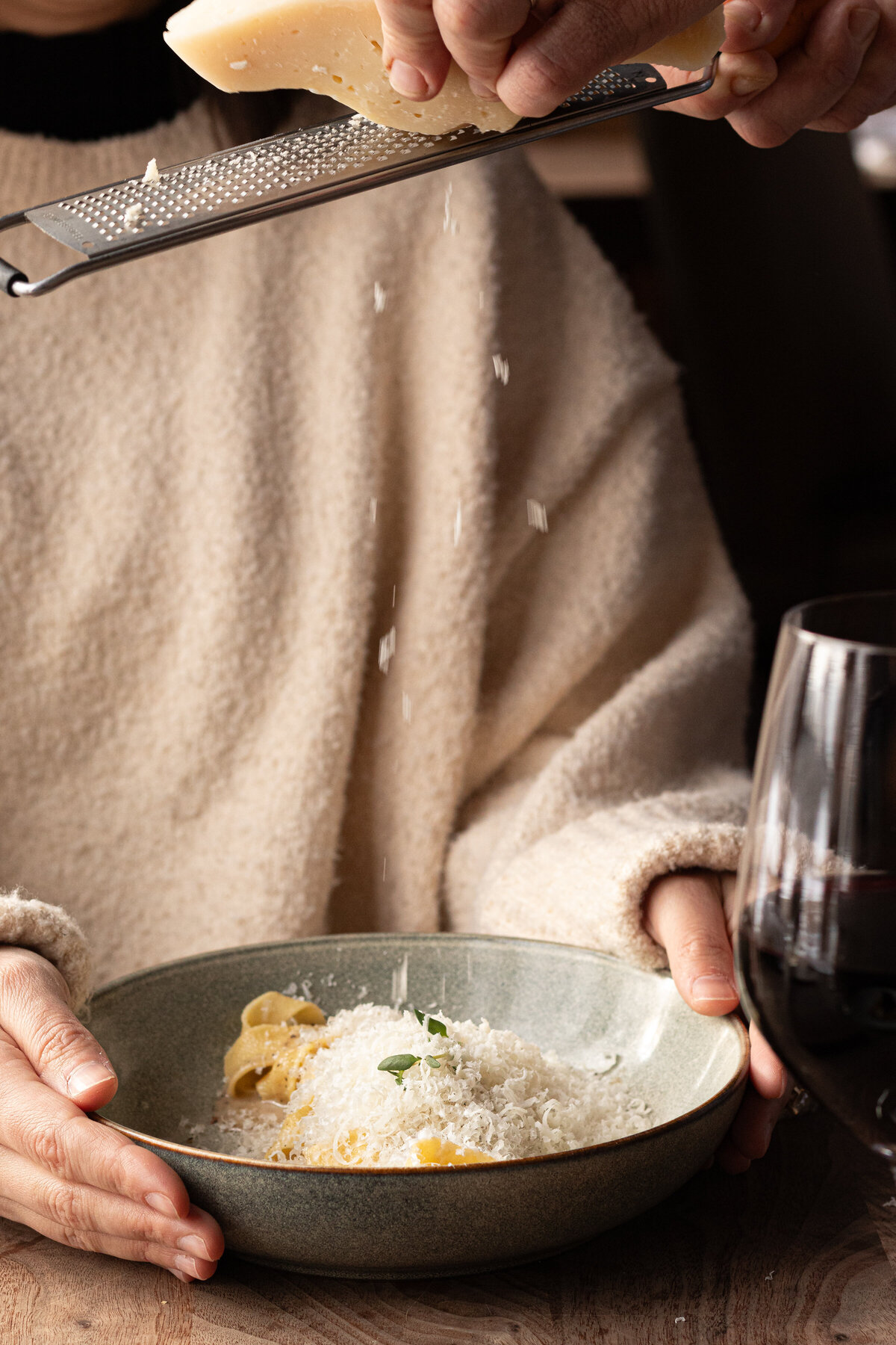 fresh cheese being grated onto a plate of pasta