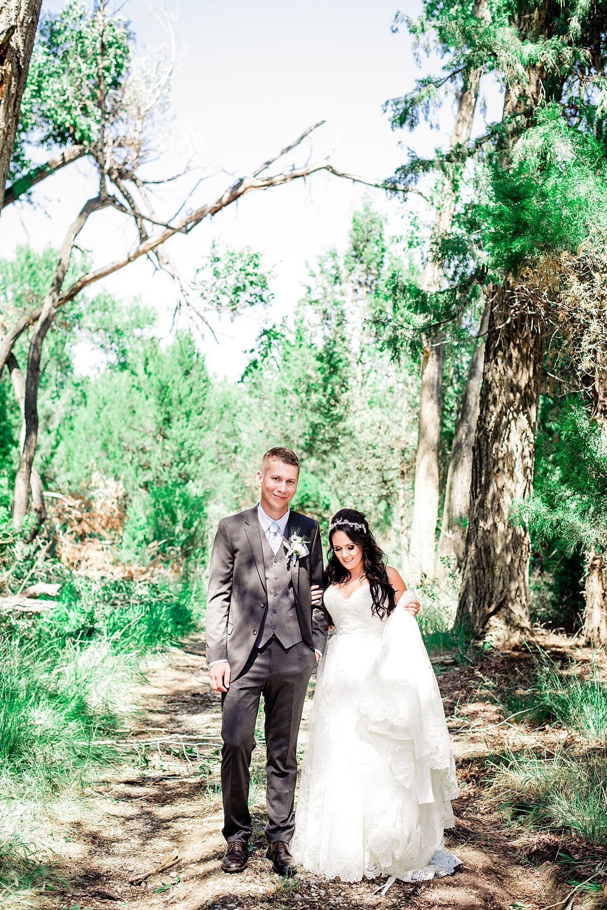 Bride and groom walking through a forested area at Headwaters Ranch on a bright sunny day