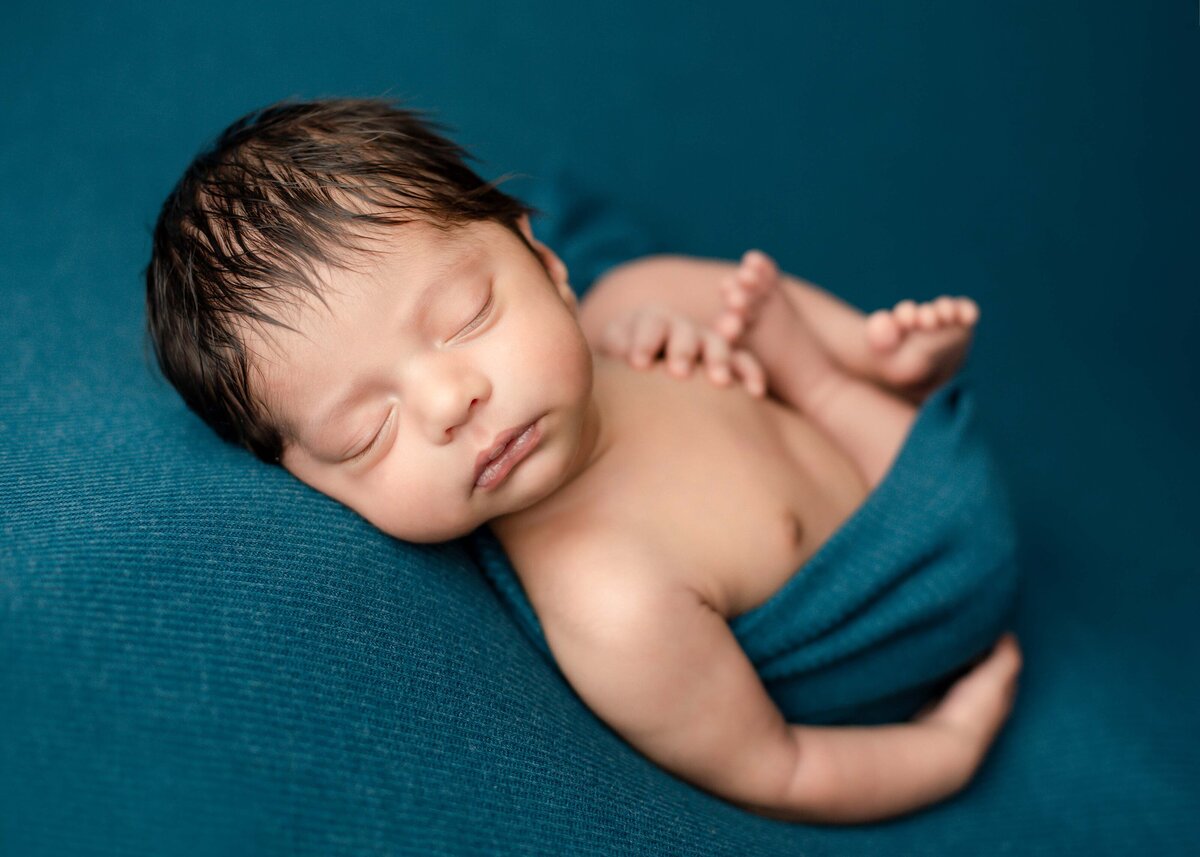 Newborn boy on a dark teal blanket wrapped up