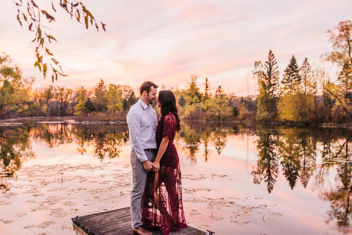 Couple holding hands and looking at each other standing on the dock of a lake