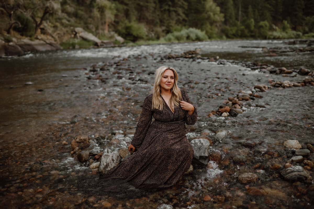 Jessica from Your Modern Story sitting on rock in  river in black dress