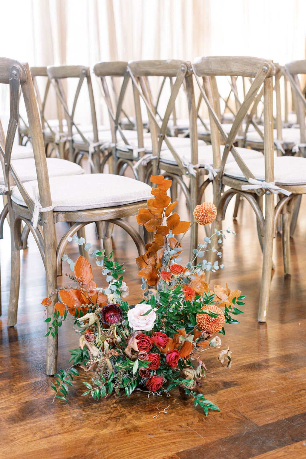 Organic ceremony aisle markers accompanied the installations with pops of burgundy, burnt orange, terra cotta, cream and fall foliage. Florals include garden roses, ranunculus, and dahlias. Floral Design by Rosemary and Finch in Nashville, TN.
