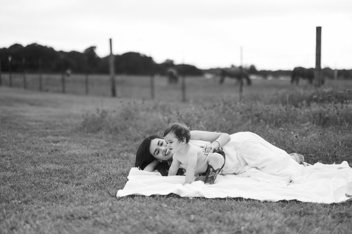 mom lays with son during milestone photos in fort worth with horses in background