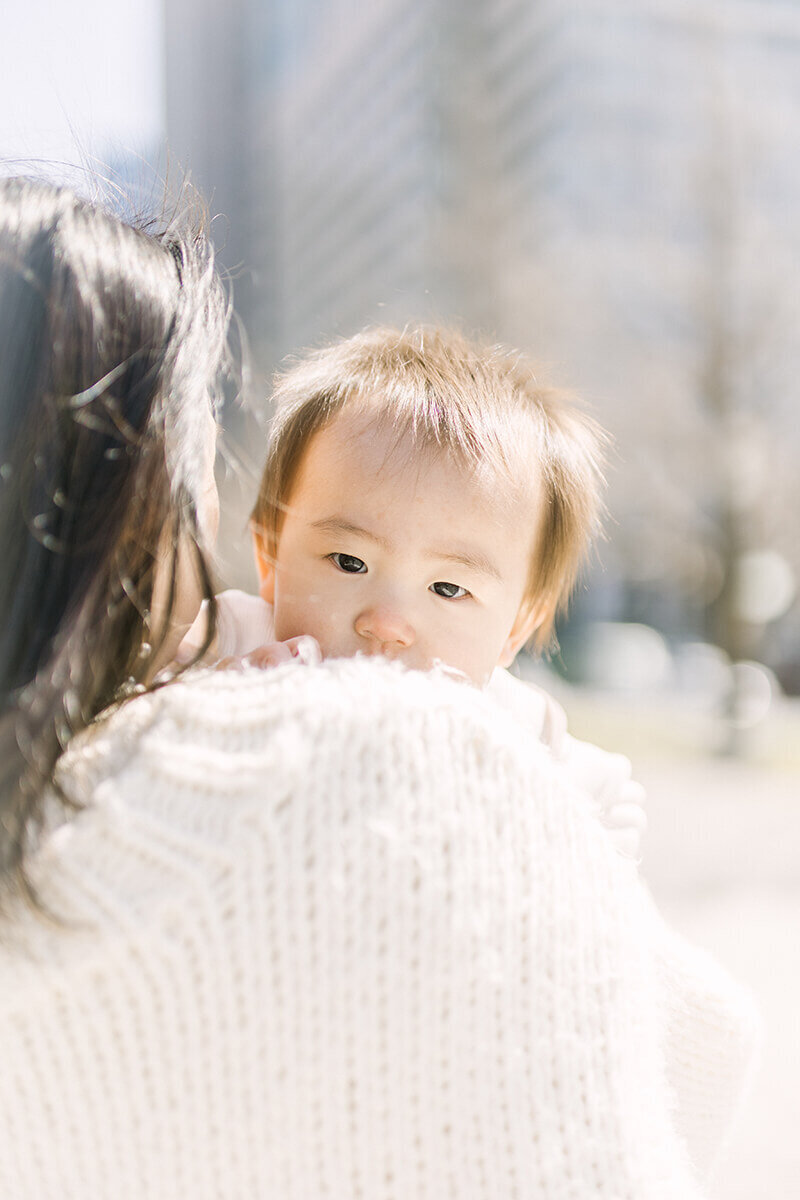 ママの肩越しに頭をのぞかせる1歳の女の子のかわいらしい写真