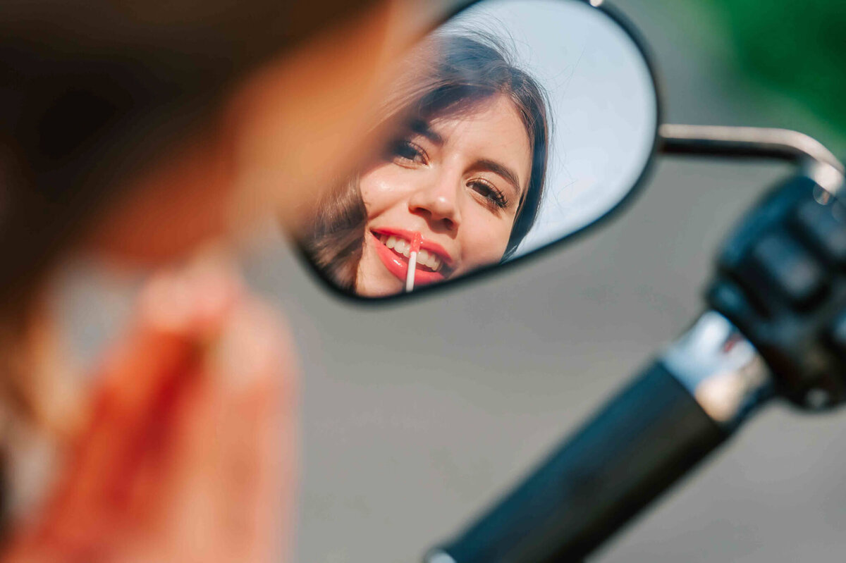 Lip gloss touch ups in the mirror of a motorcycle. 