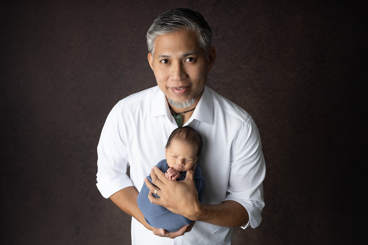 Proud dad cradling newborn wrapped in blue, captured by Texas Newborn Photographer Lindsay Walden.