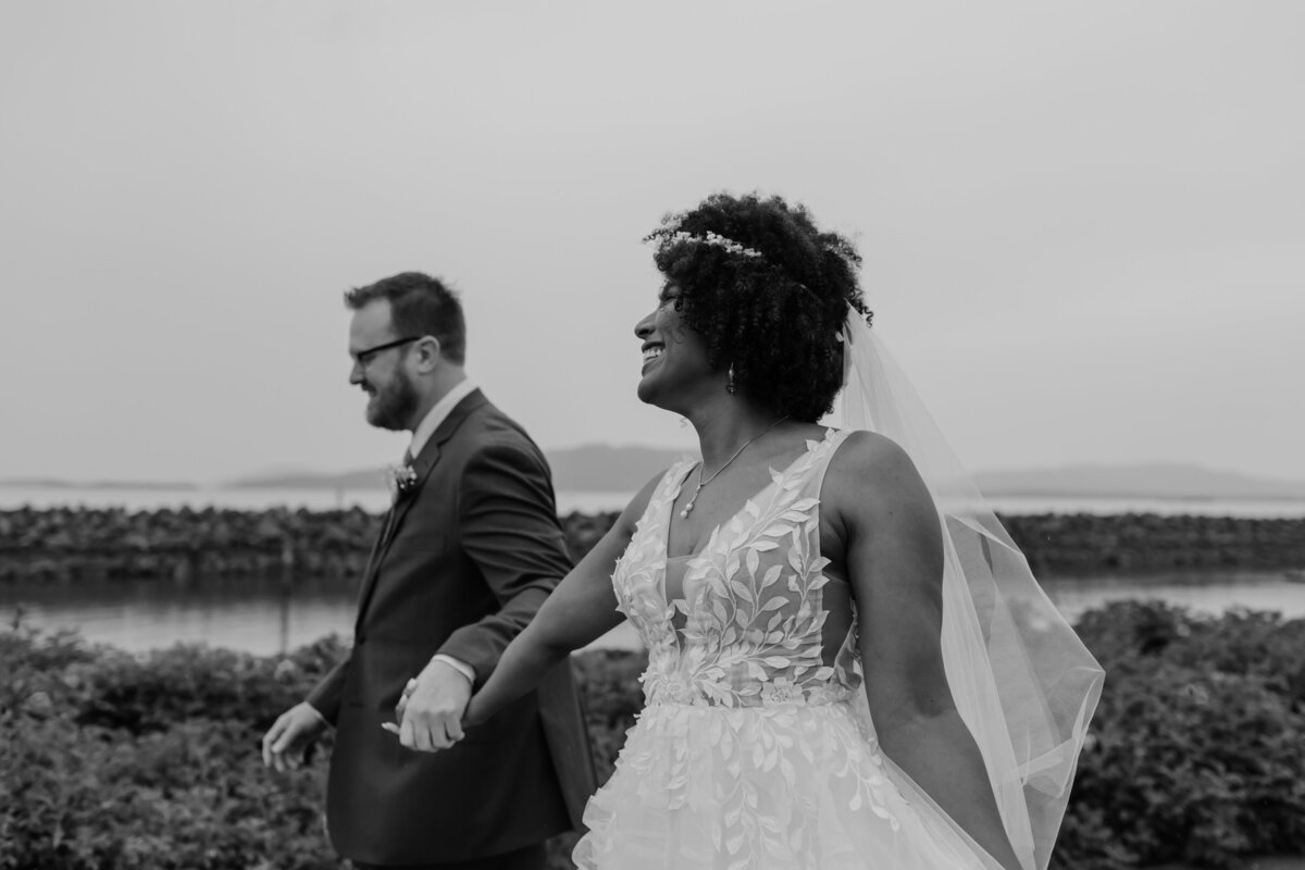 A playful candid of a bride and groom walking along a waterfront. Captured by Fort Worth Wedding Photographer, Megan Christine Studio