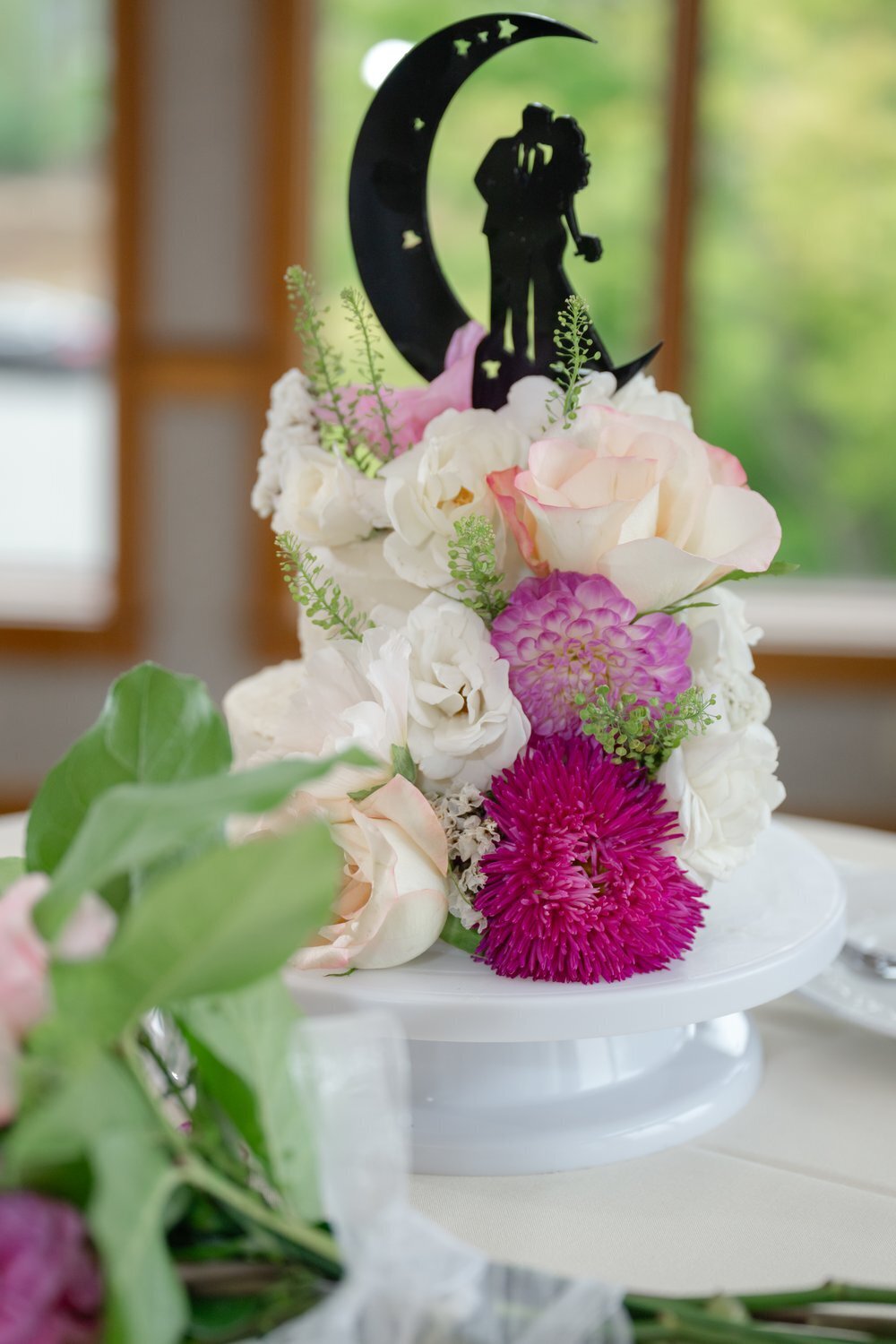 wedding cake with pink and white flowers and crescent moon topper