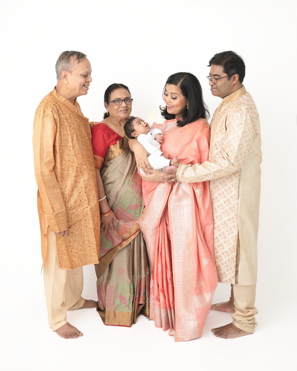 extended family with new baby in white studio portrait wearing traditional Indian clothing