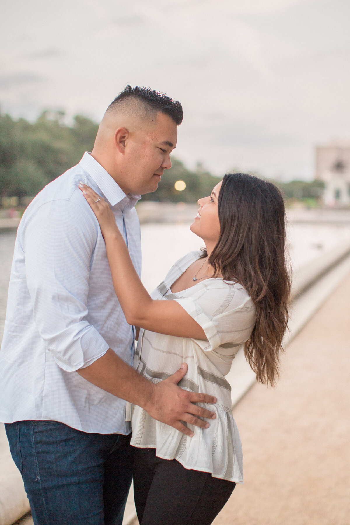 A couple look lovingly into each other's eyes while posing in front of a water feature.