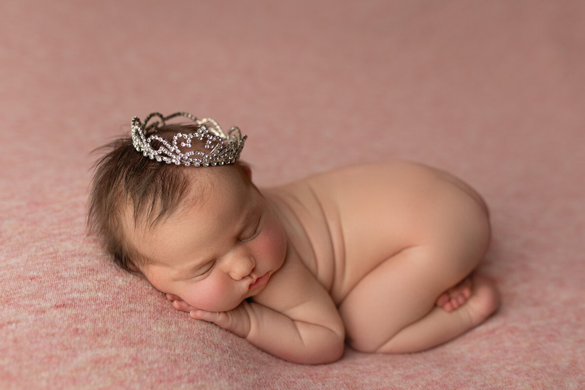 Baby girl in tushy up newborn pose wearing a crown.
