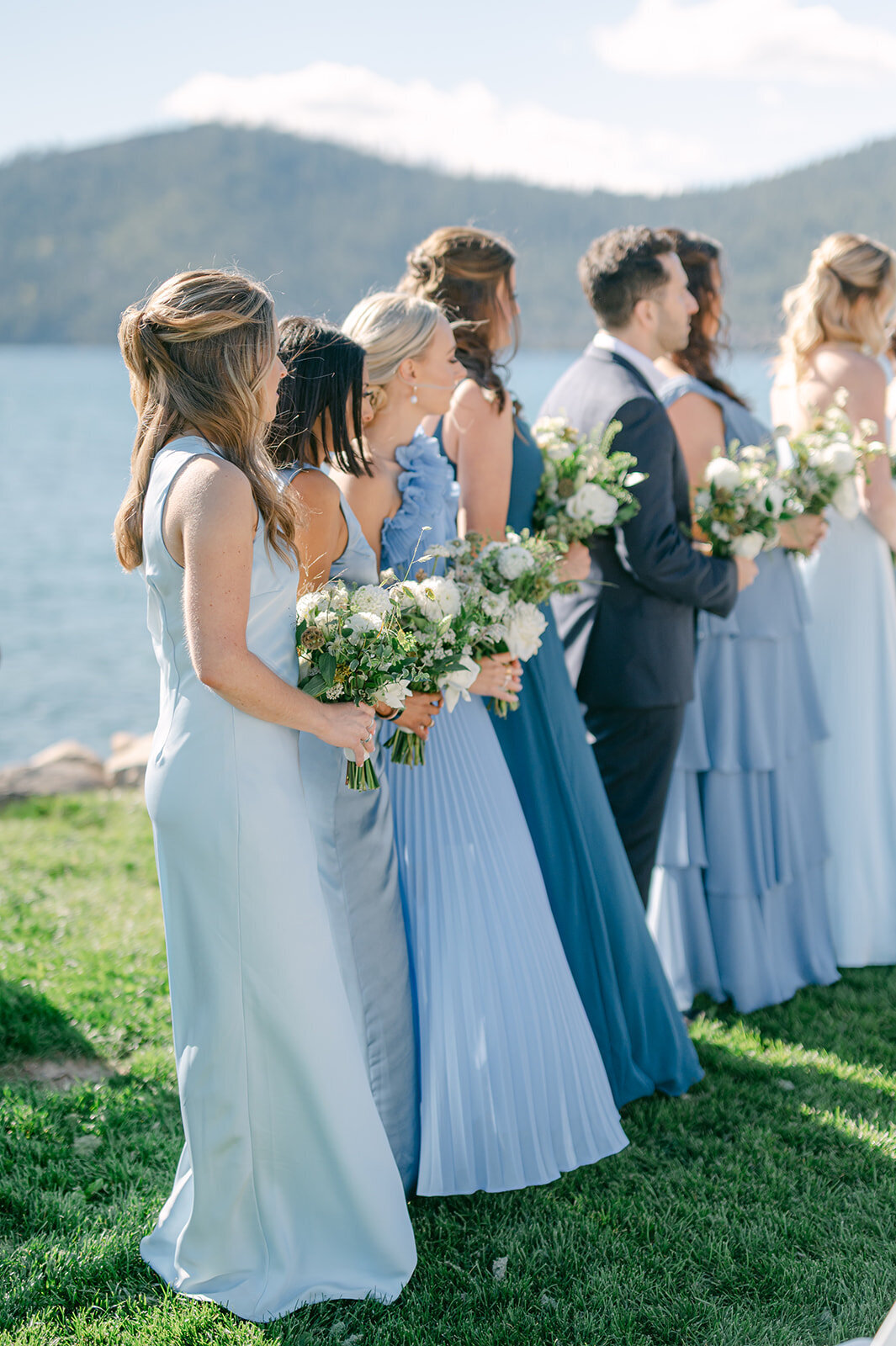 Bridesmaids in blue dresses stand lakeside at ceremony site during Lake Tahoe Wedding.