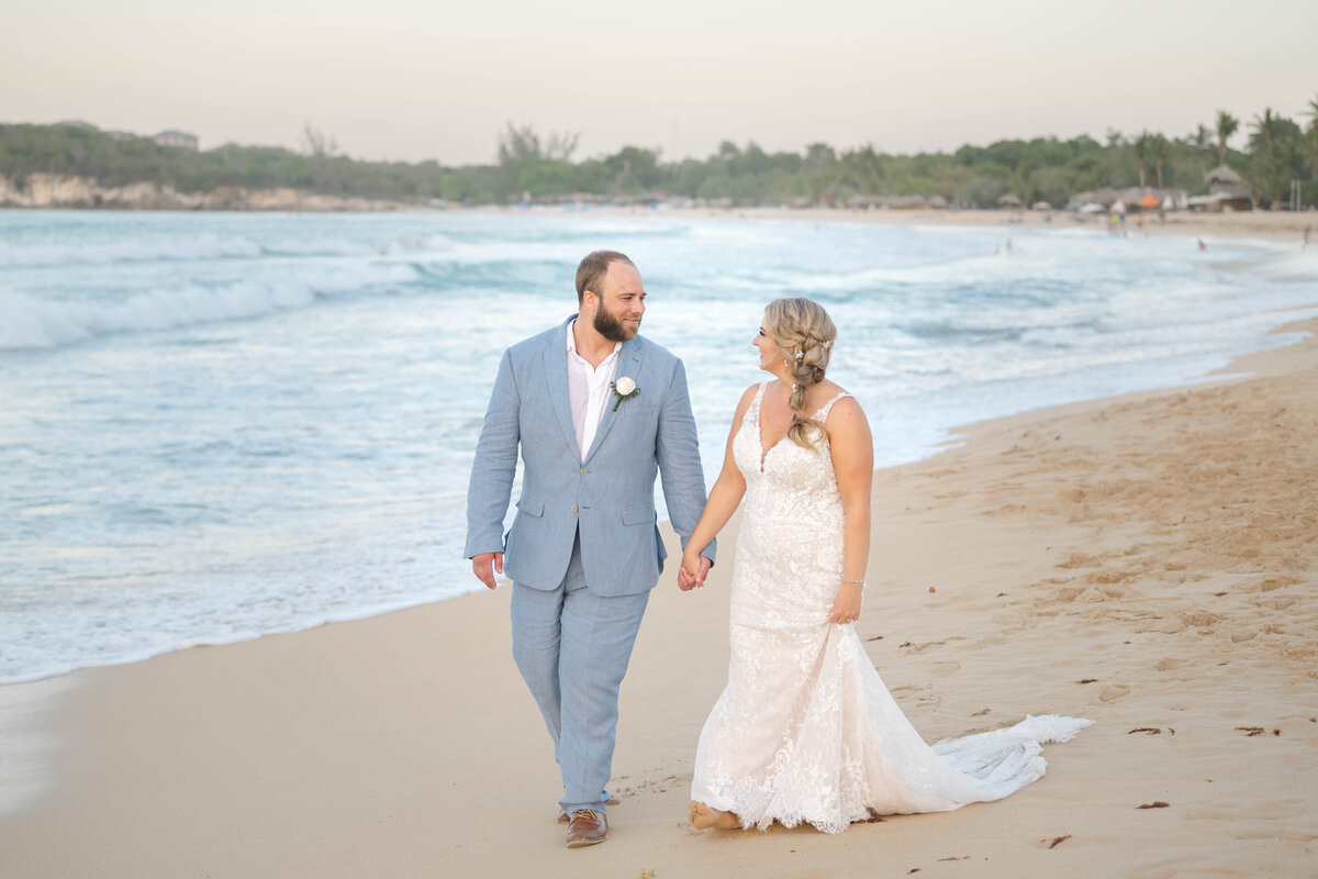 a bride and groom walking on the beach at Dreams Macao Punta Cana