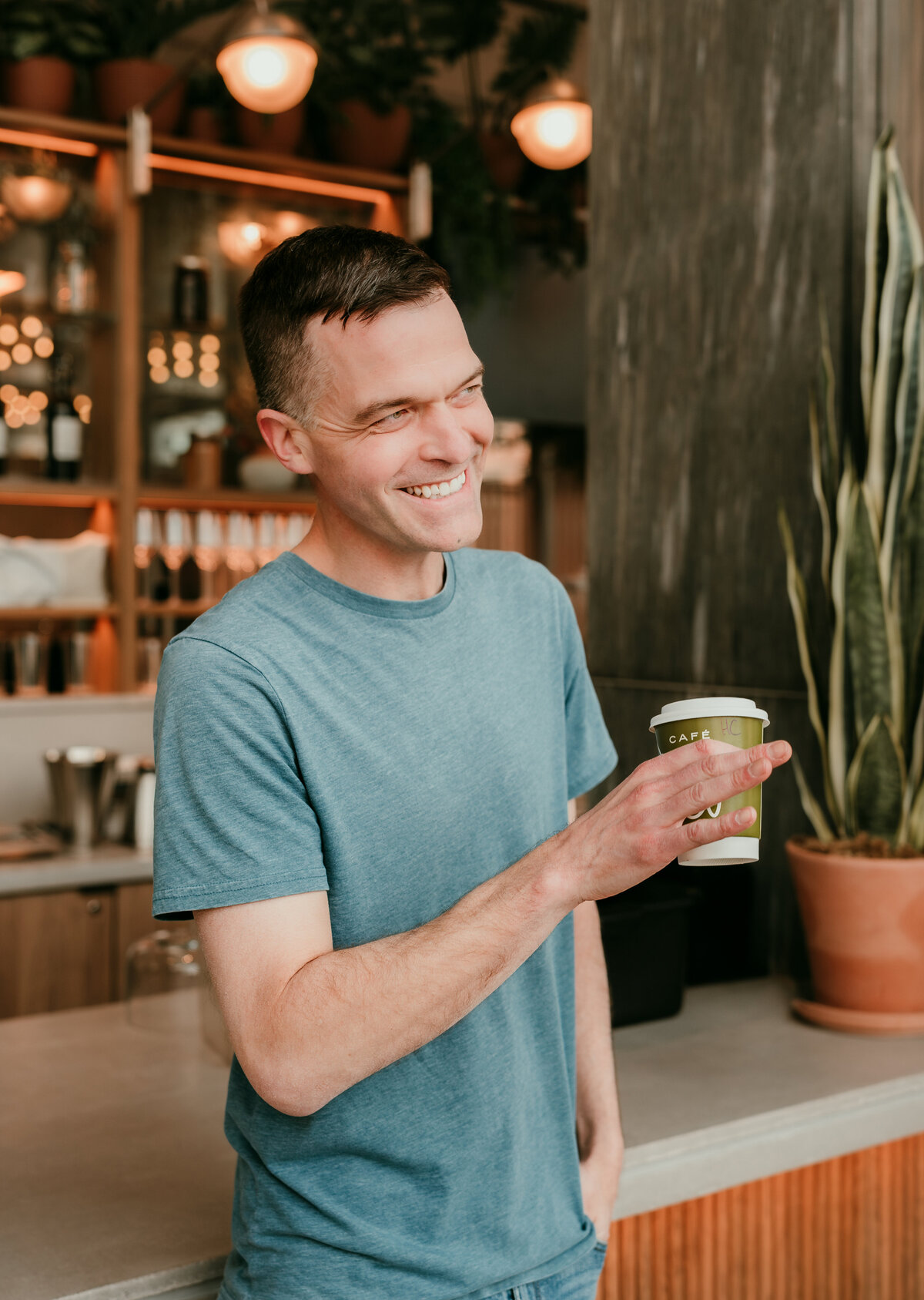 Man smiling and holding a drink in a trendy café setting, highlighting a friendly and approachable vibe for online dating.