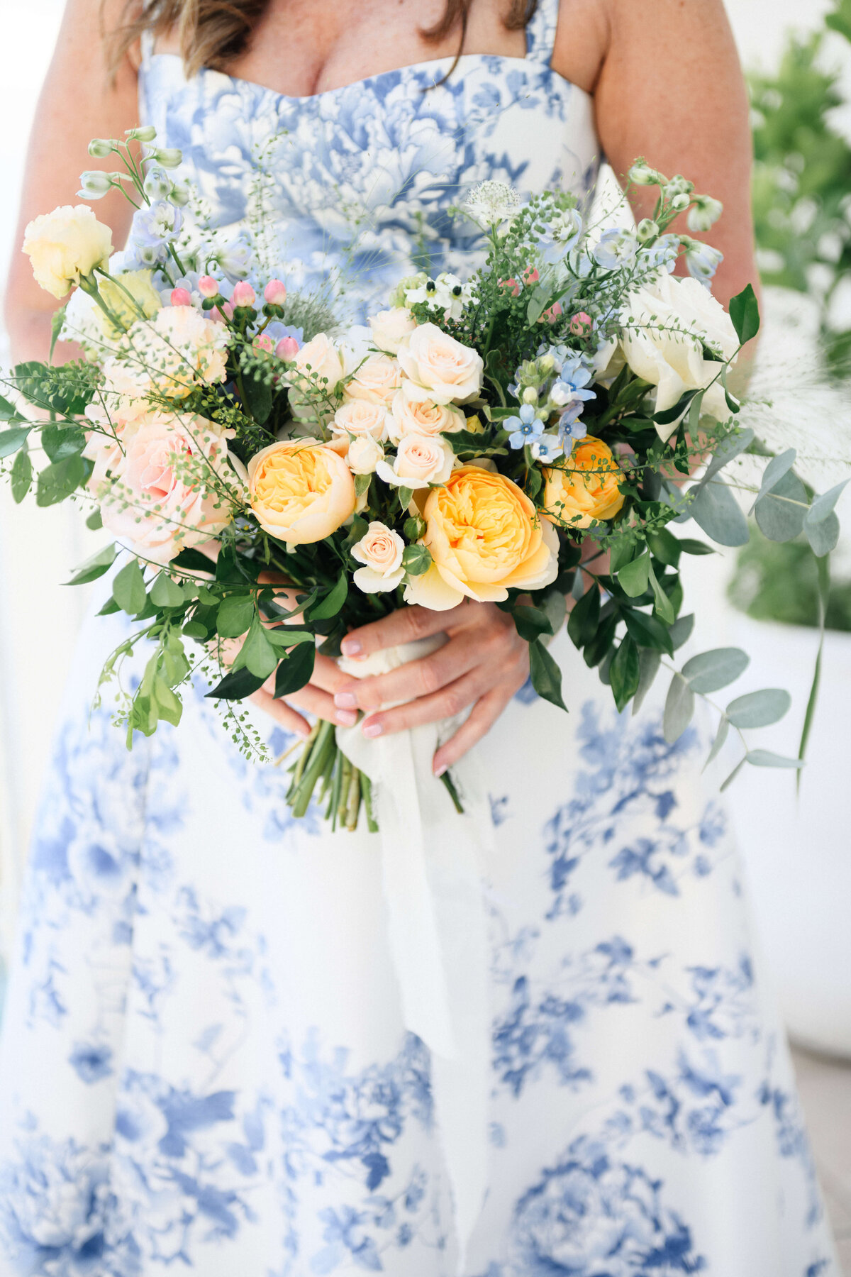 Peach and yellow bridal bouquet, with the bride in a blue floral dress