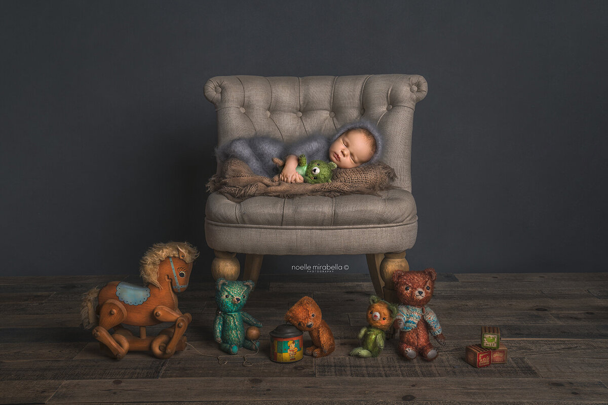 Newborn baby sleeping on a vintage chair surrounded by vintage toys.
