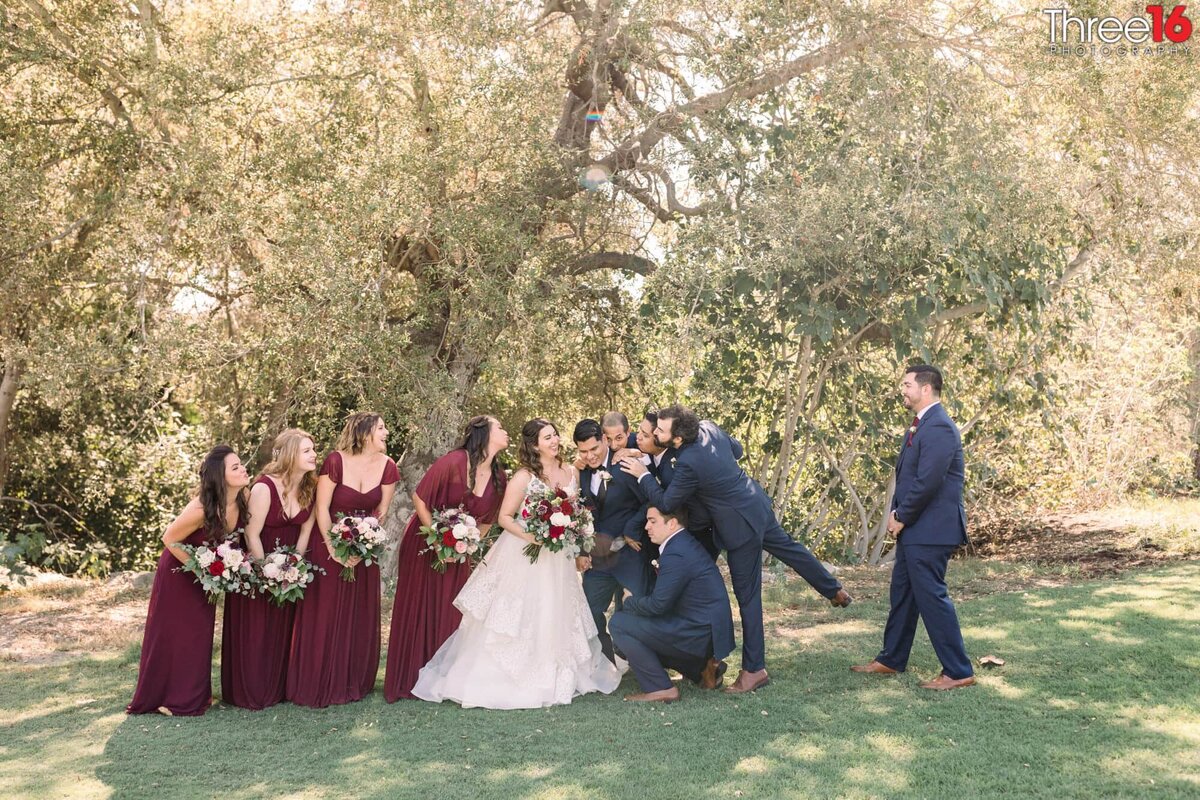 Bridal Party makes kissy faces at the Groom who is laughing