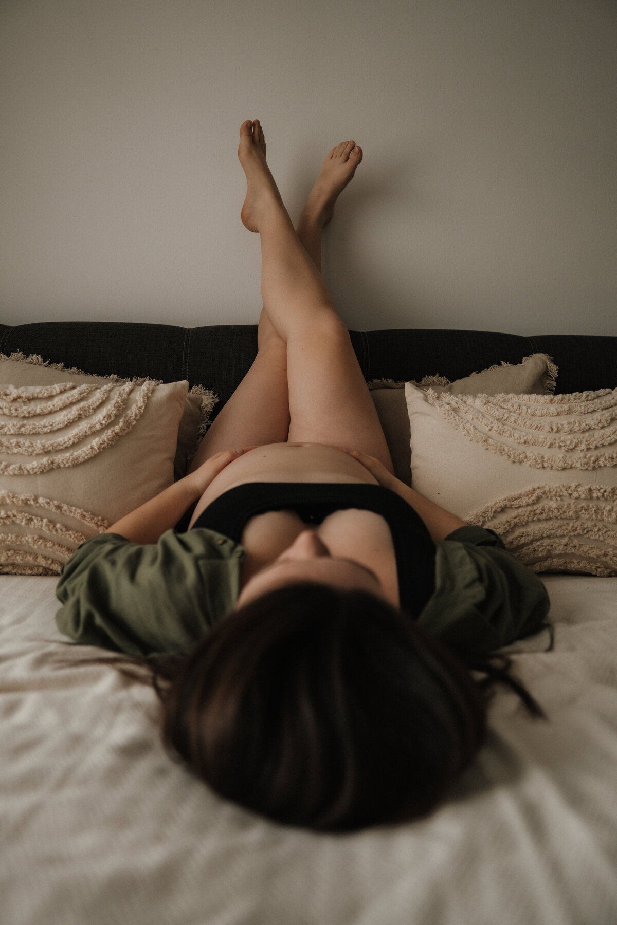 Schwangere liegt mit dem Rücken auf dem Bett und überkreuzt an der Wand die Beine