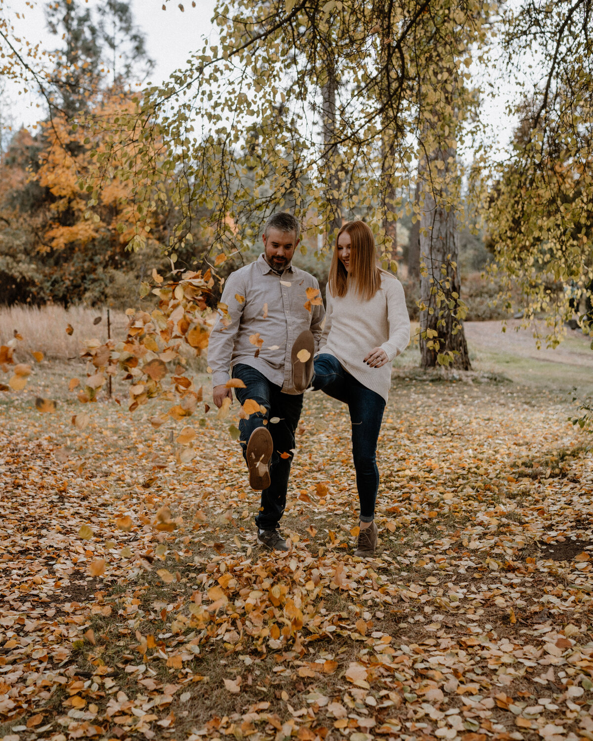 A fall couple laughs and runs through a field during their playful engagement session in Spokane, Washington, highlighting joy and spontaneity.