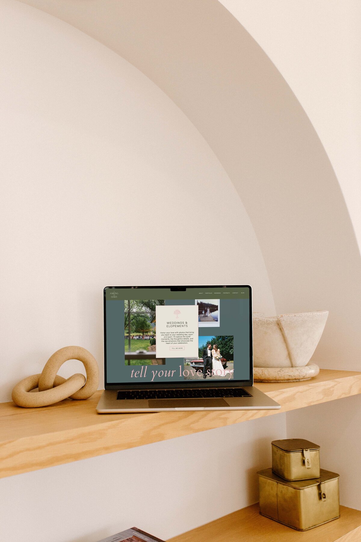 A laptop sits open and shows a website for a wedding photographer with photos and text that reads tell your love story.