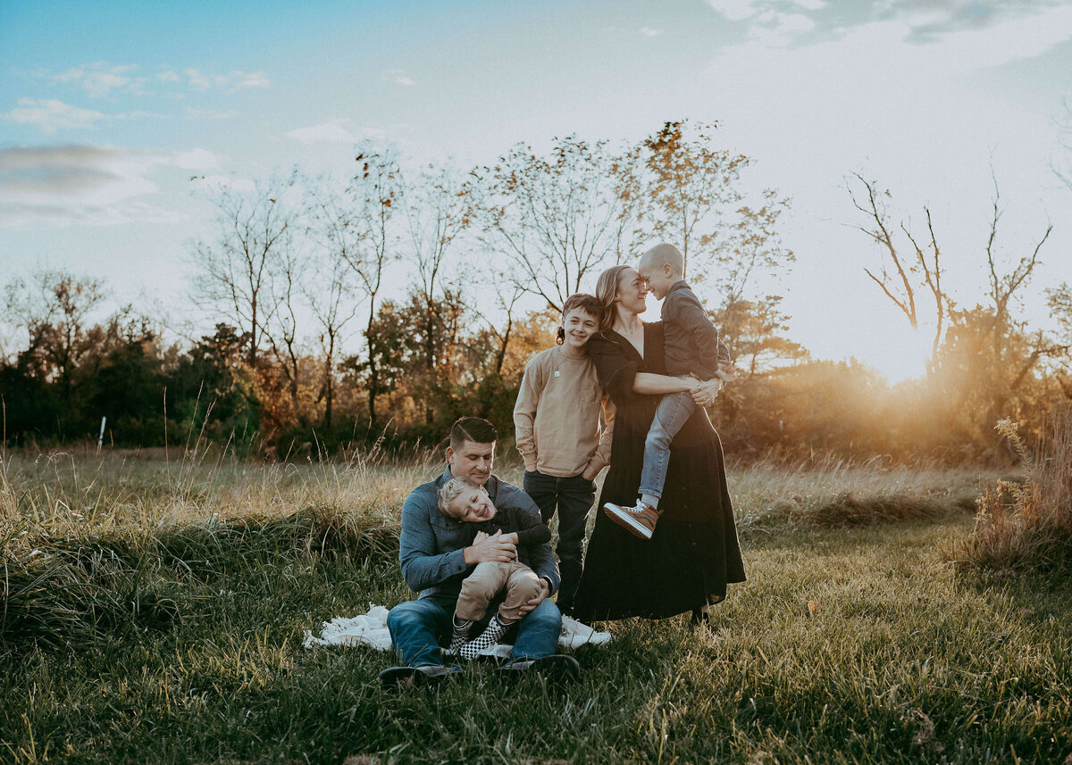 A family of five organically poses with their gorgeous family farm in the background during a sunset session in Denver, Colorado.