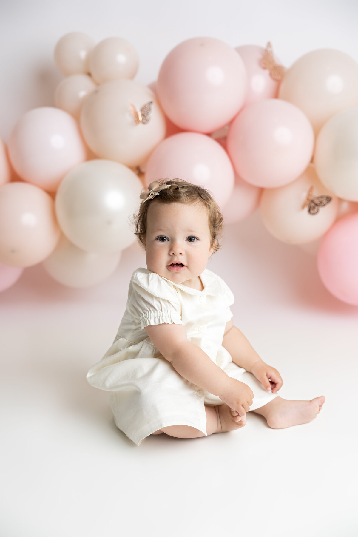 Baby girl cake smash with pink and white balloons, butterflies, and pink cake