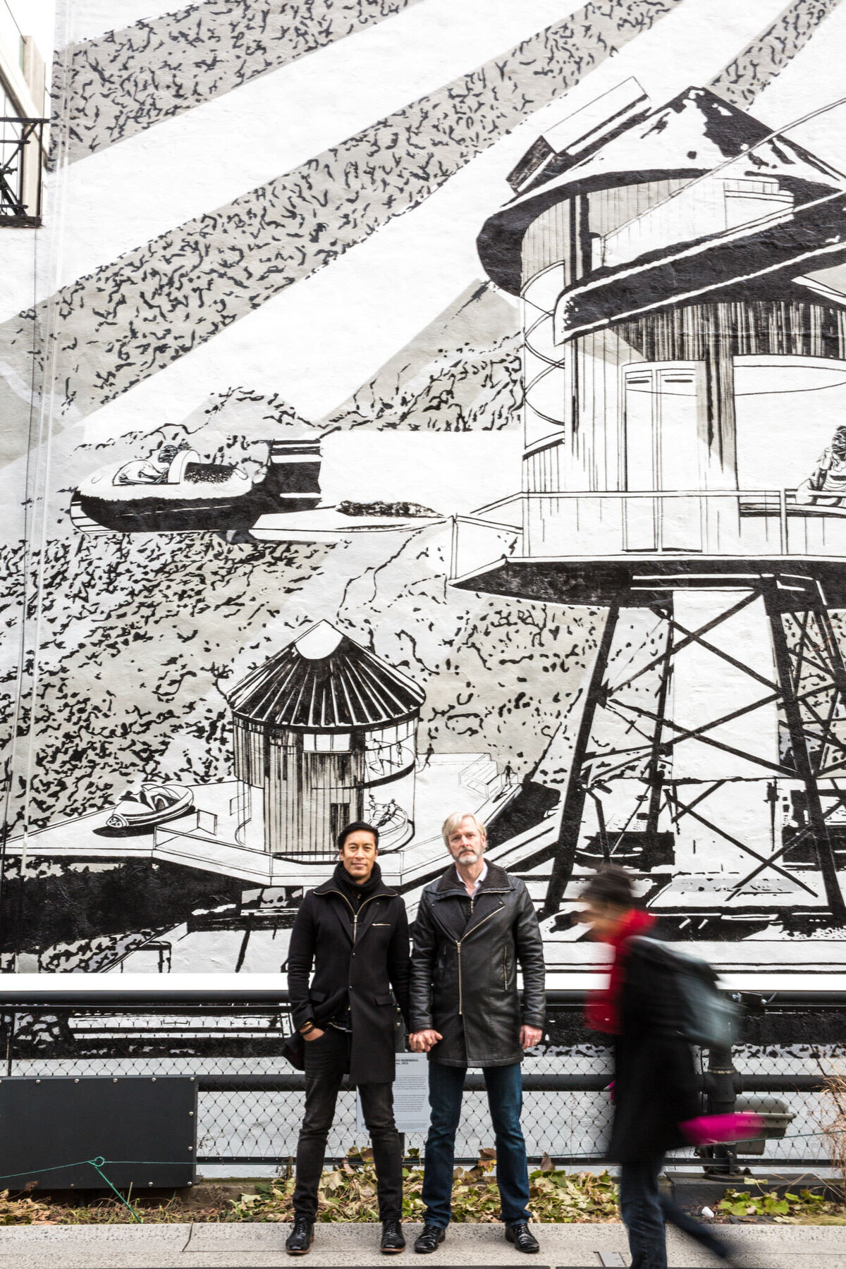 A couple holding hands in front of a black and white mural .