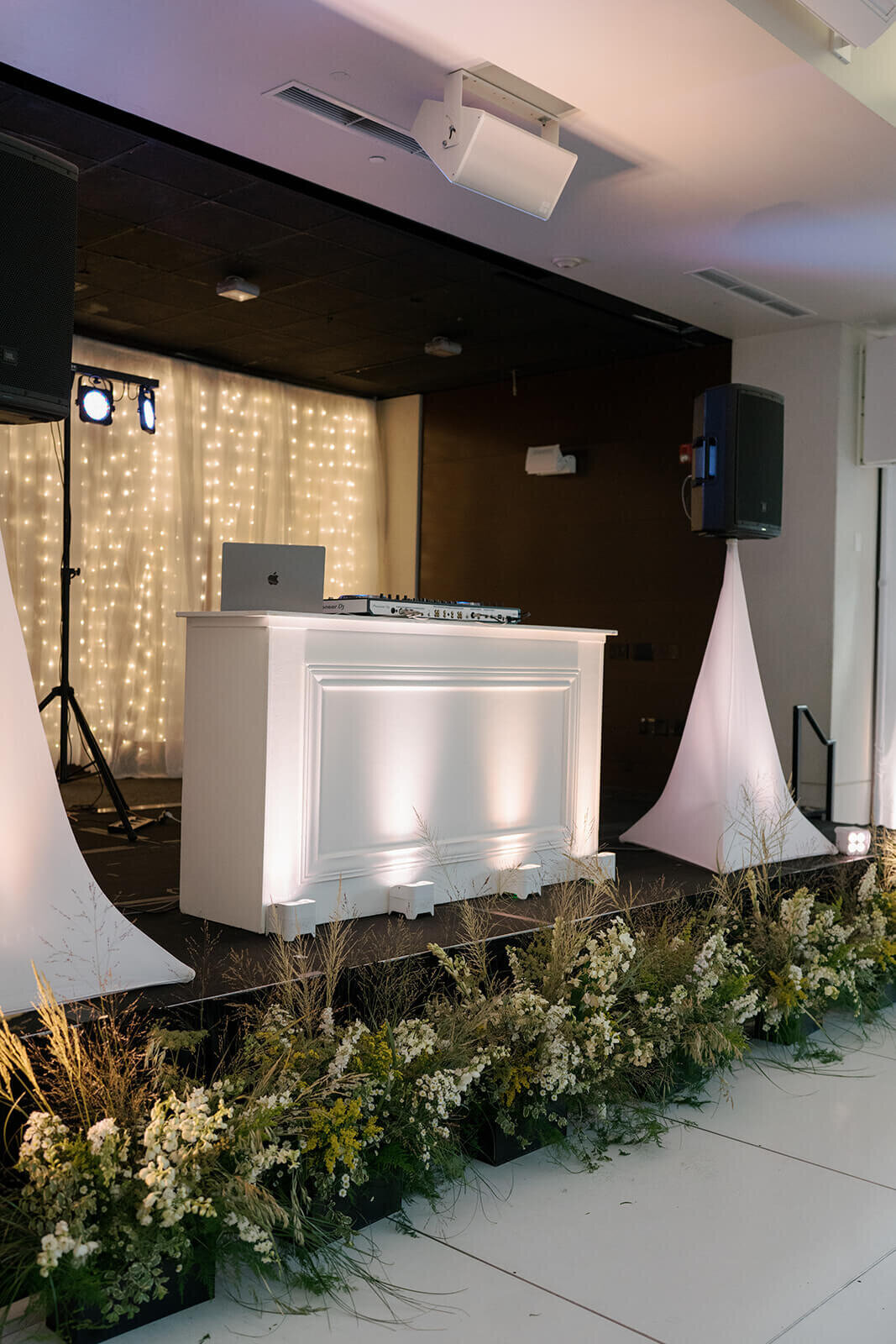 A DJ booth with sparkling string lights in the background and beautiful greenery below at the Aspen Meadows Resort wedding reception.