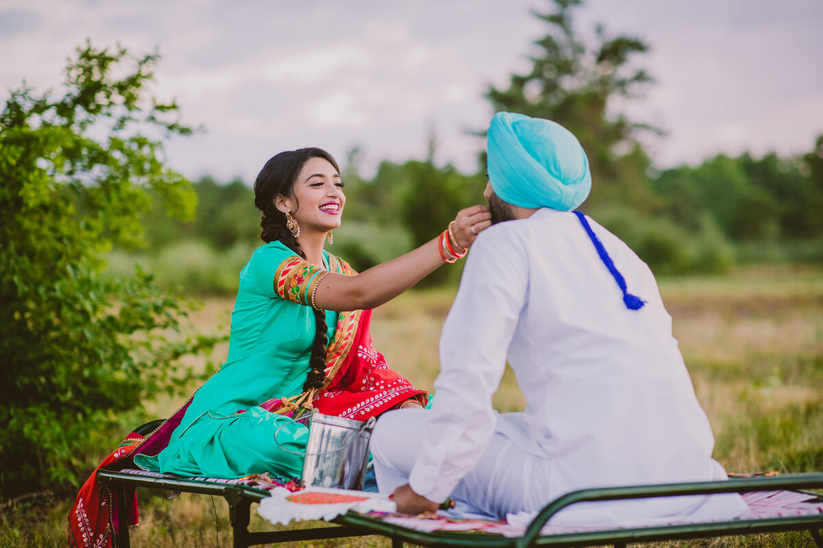 sikh bride feeding the groom during their traditional punjabi-themed engagement session while sitting on a manja