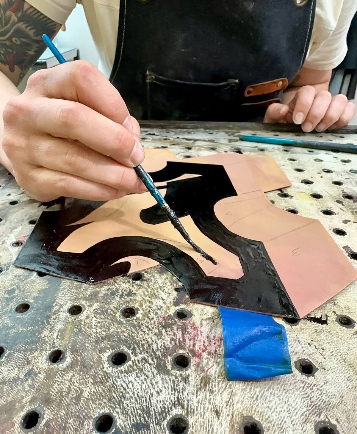 An artist painting detailed black asphaltum patterns on a copper plate, demonstrating care in tonal separation.