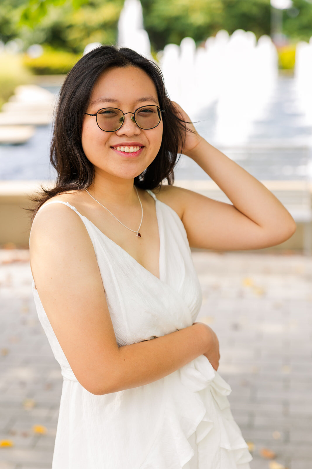 close up of high school girl with sun glasses standing in front of a fountain one hand in her hear in Atlanta Sandy Springs