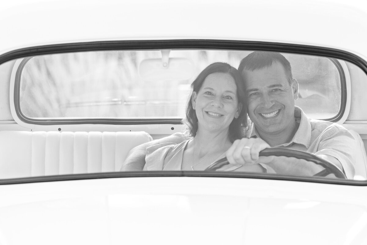 Father and a mother sitting together and smiling in the front of a white truck outdoors in North East, PA.