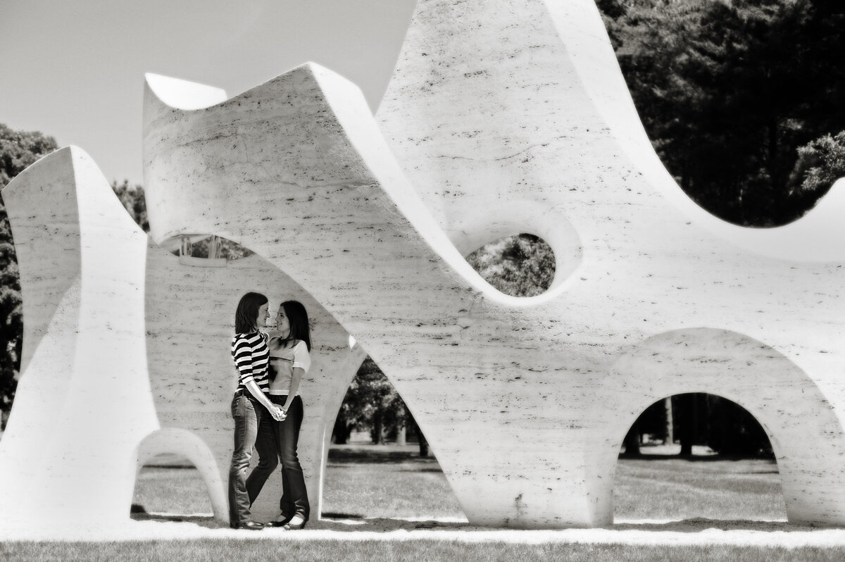 A couple standing together and holding hands under a sculpture 