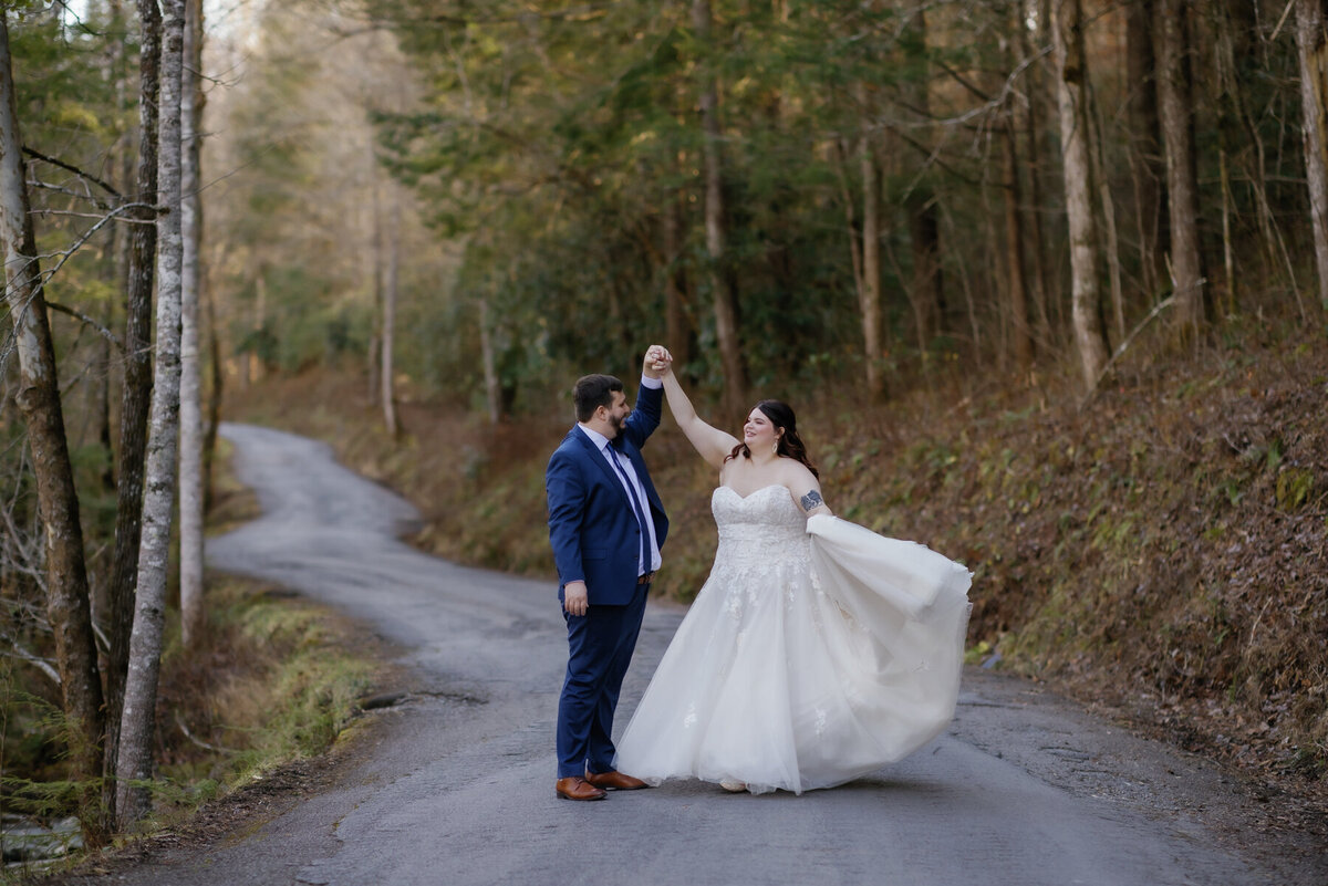 Smoky mountain elopement in the woods with groom twirling his bride as they dance together on a path in the woods