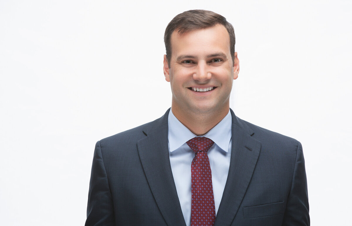 A male professional in a grey suit and red tie poses for a corporate business headshot on a high key white background at Janel Lee Photography studios in Cincinnati Ohio