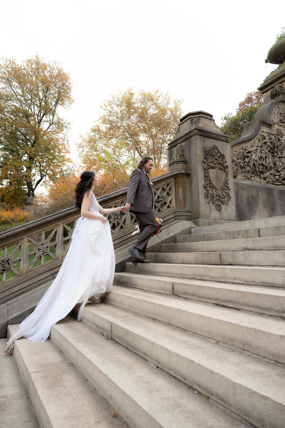 Bride and groom walking up historic stone steps in Central Park, NYC, surrounded by golden fall foliage during their intimate elopement.