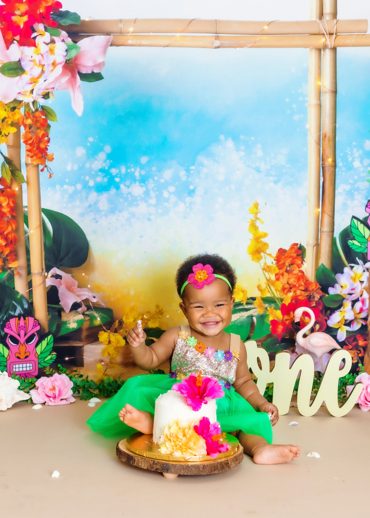 Cake Smash Photographer, a one year old baby sits before a floral cake in a floral dress and tropical background