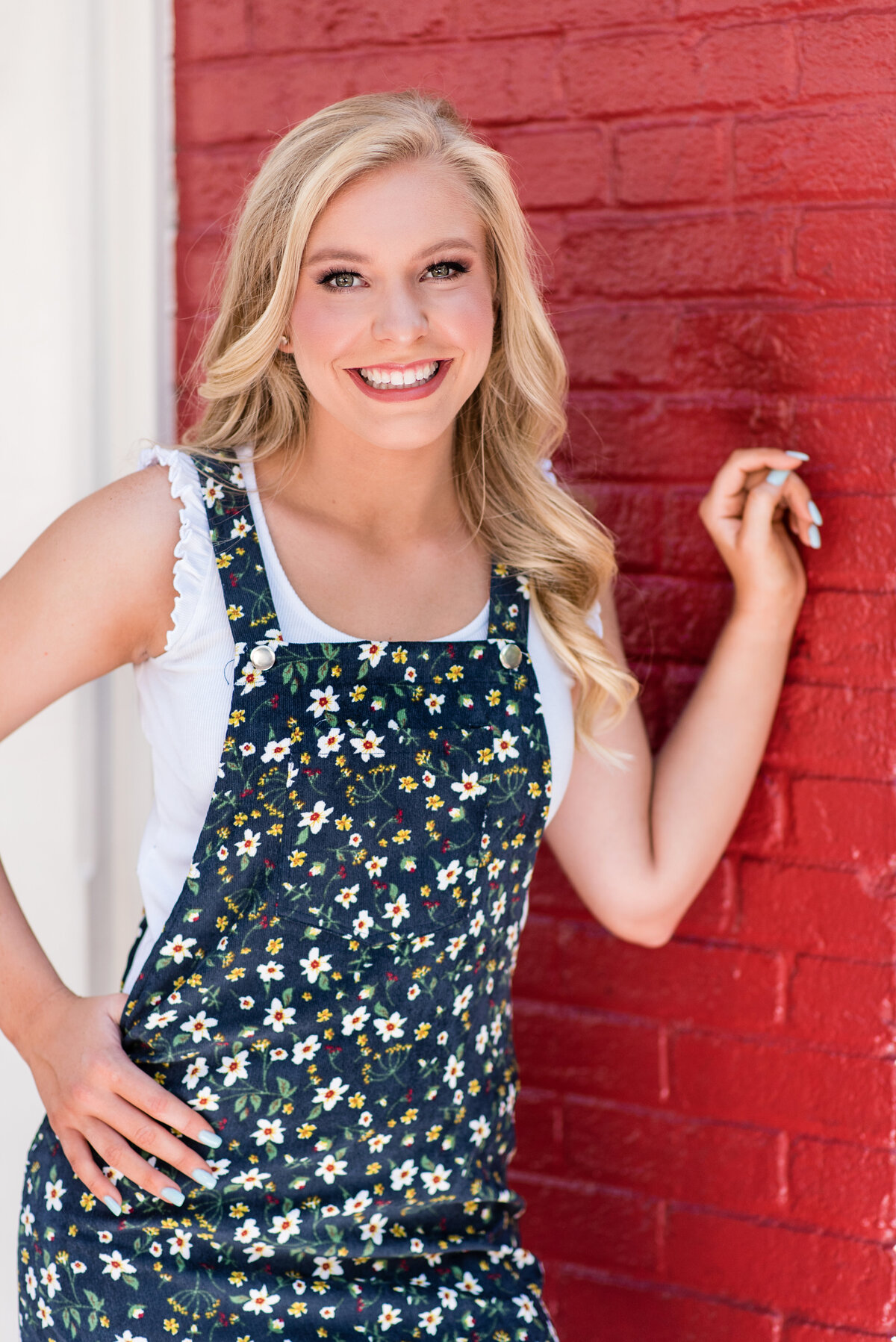 Richmond senior girl poses in front of red brick wall during senior portrait session.