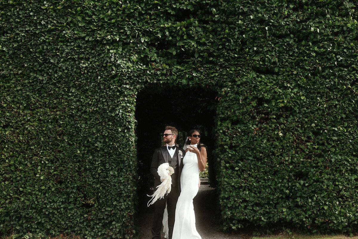 Bride and groom standing under greenery arch at Killruddery House and Gardens, Wicklow
