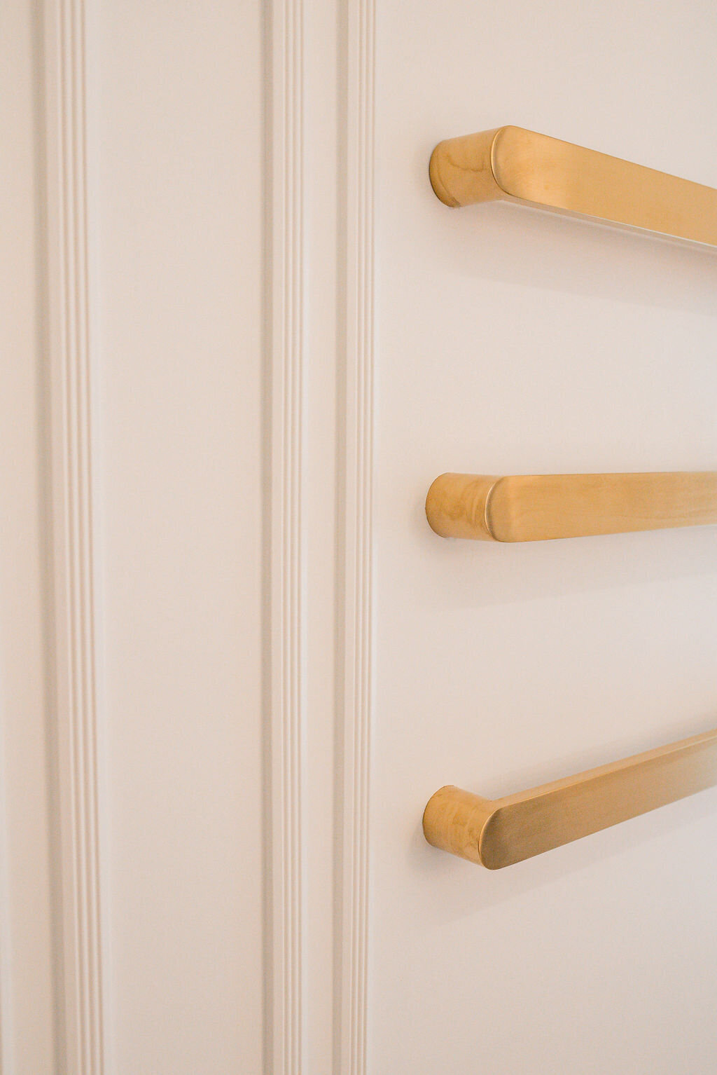 A close-up look at the white walls and crown molding in a modern bathroom. Chic gold towel bars are visible.