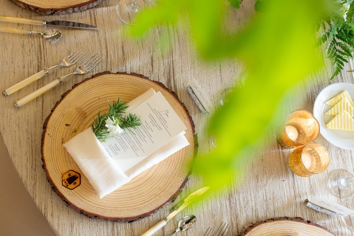 place setting for wedding reception with wooden charger plate, ivory napkin, and a greenery bundle