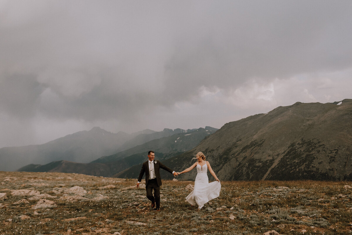 bride and groom running theough open field with iconic mountain views in colorado