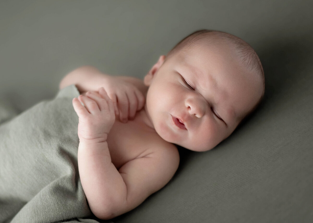 A newborn makes a sour face while laying on back on green pad