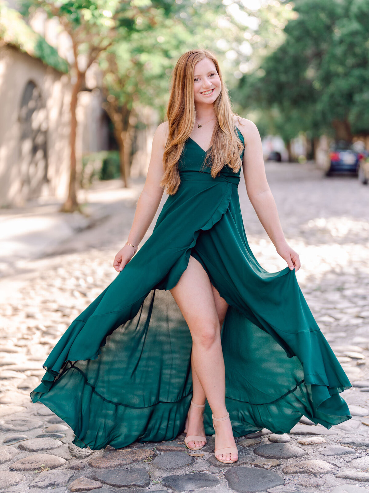 Senior girl in emerald gown sitting near tree roots in wooded Charleston setting